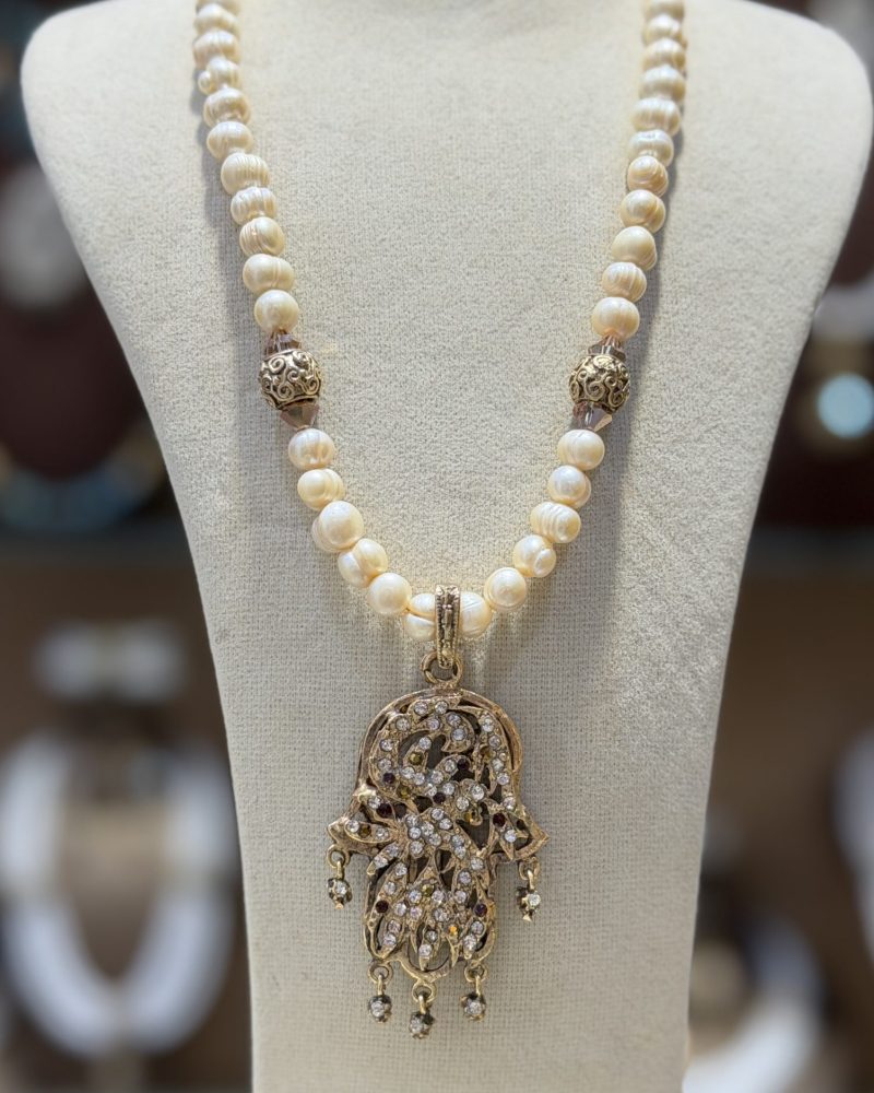 Collier Main de Fatma Lalla Jasmine en perles de culture avec pendentif Khamssa doré, cristaux scintillants et breloques mobiles inspirés de la joaillerie algérienne.