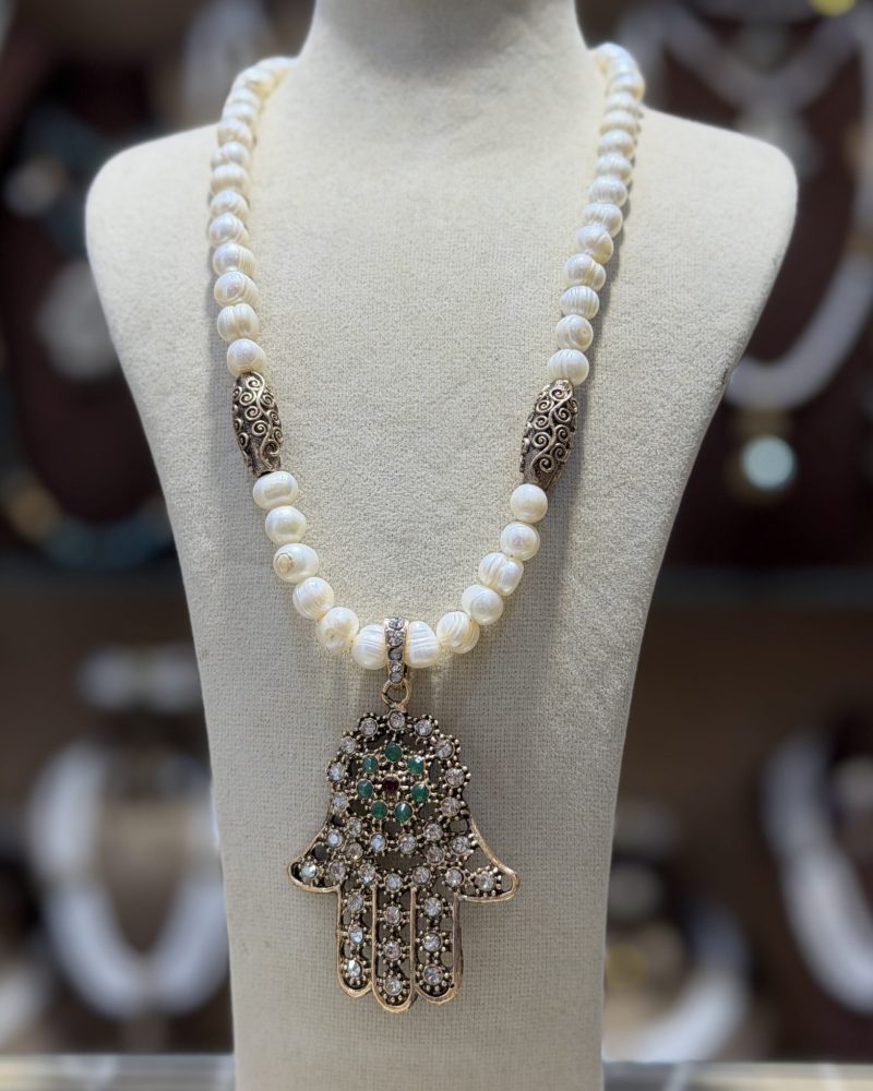 Collier Khamssa en perles de culture avec pendentif Main de Fatma doré orné de cristaux scintillants et de pierres vertes, bijou inspiré de la joaillerie traditionnelle algérienne