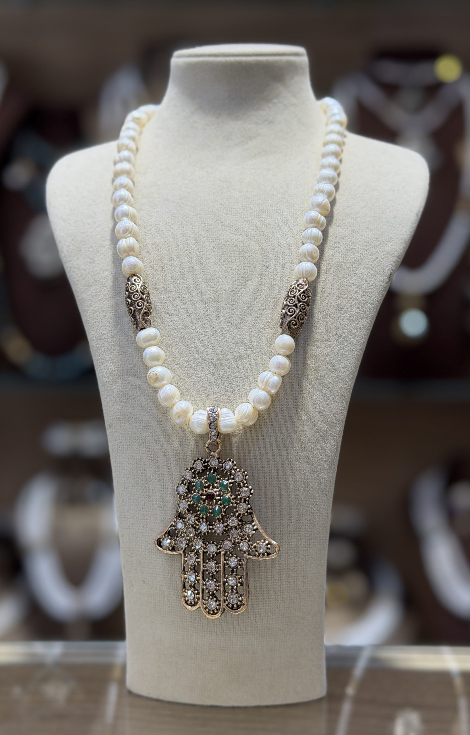 main de fatma Collier Khamssa en perles de culture avec pendentif Main de Fatma doré orné de cristaux scintillants et de pierres vertes, bijou inspiré de la joaillerie traditionnelle algérienne