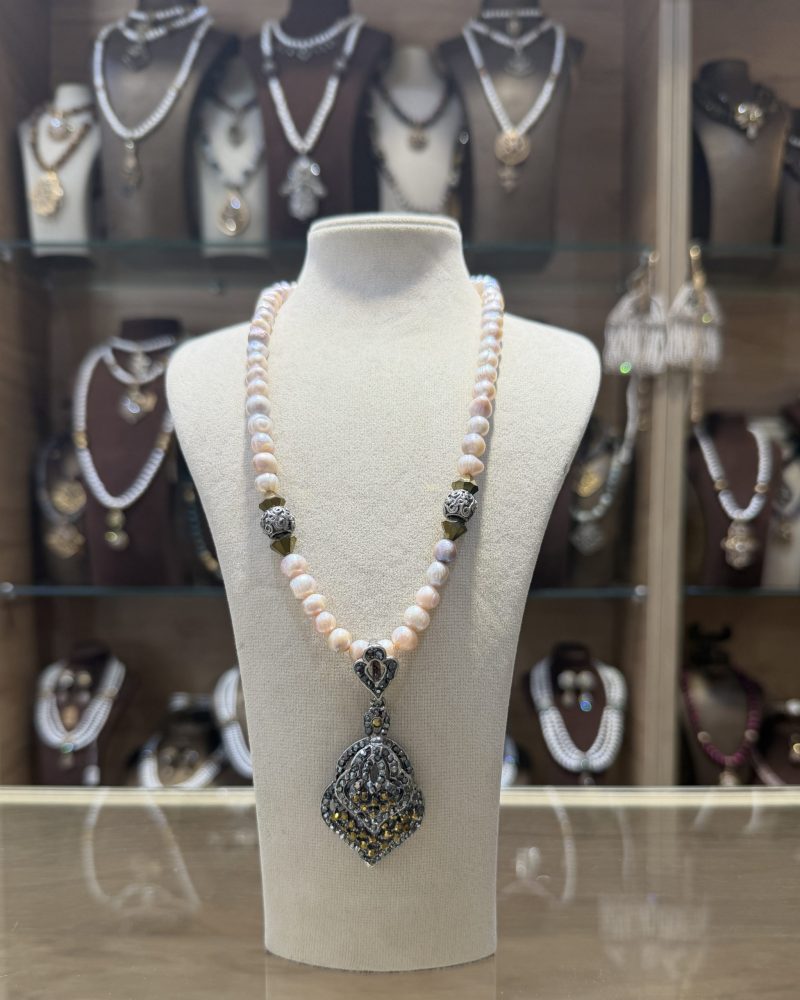 Collier Pique doré traditionnel avec un rang de perles de culture aux reflets roses et un pendentif ciselé en bronze pavé de cristaux