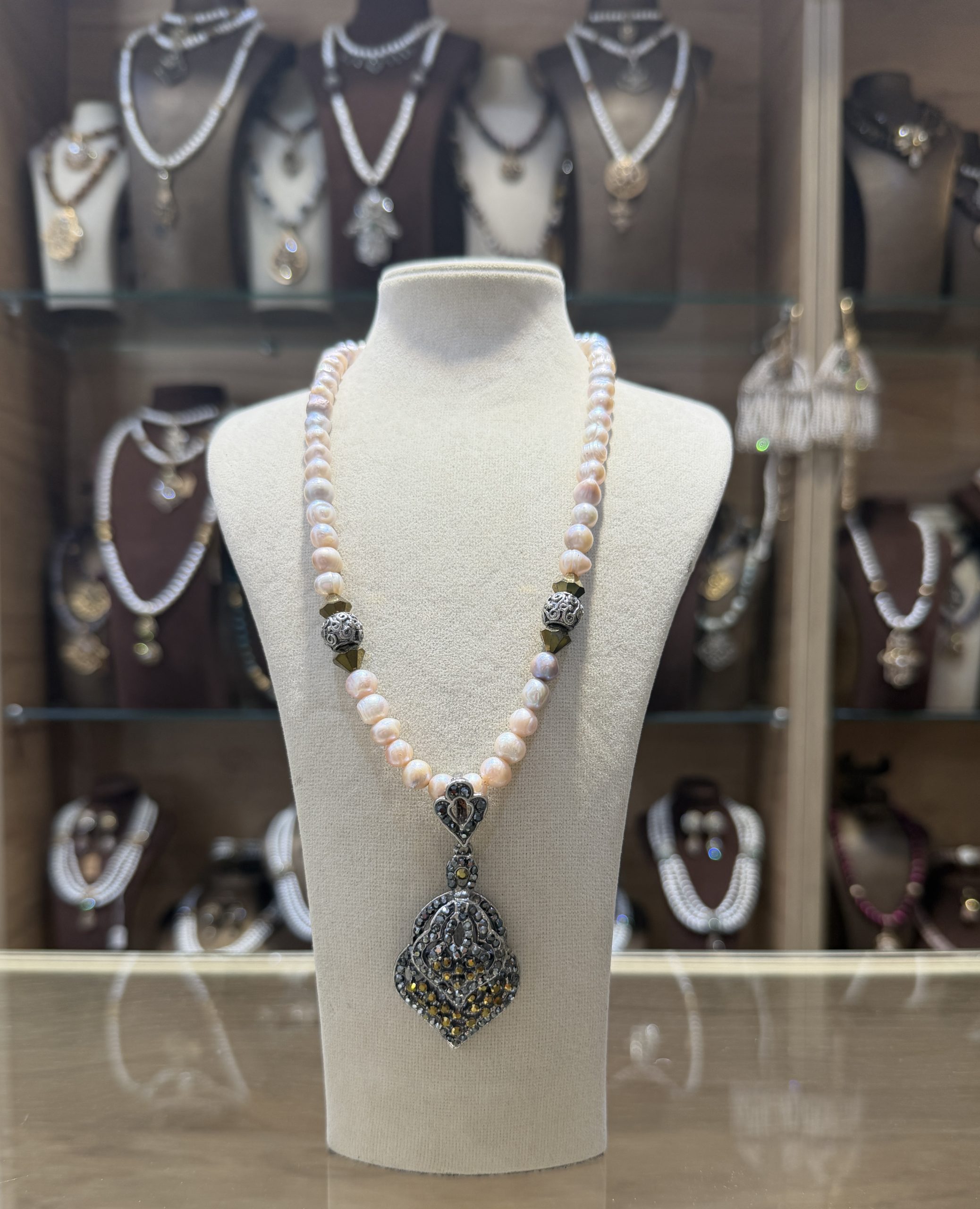 collier-pique-dore-perles-roses Collier Pique doré traditionnel avec un rang de perles de culture aux reflets roses et un pendentif ciselé en bronze pavé de cristaux