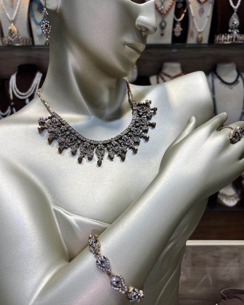 Parure Lalla Farihene comprenant un collier en draperie de cristaux clairs, un bracelet maillons, des boucles d'oreilles et une bague en bronze traité à l'or