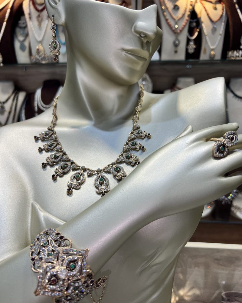 Parure Bahdja Royale 4 pièces comprenant un collier en pampilles ciselées, une manchette large, des boucles d'oreilles et une bague en bronze traité à l'or avec cristaux verts et bordeaux,