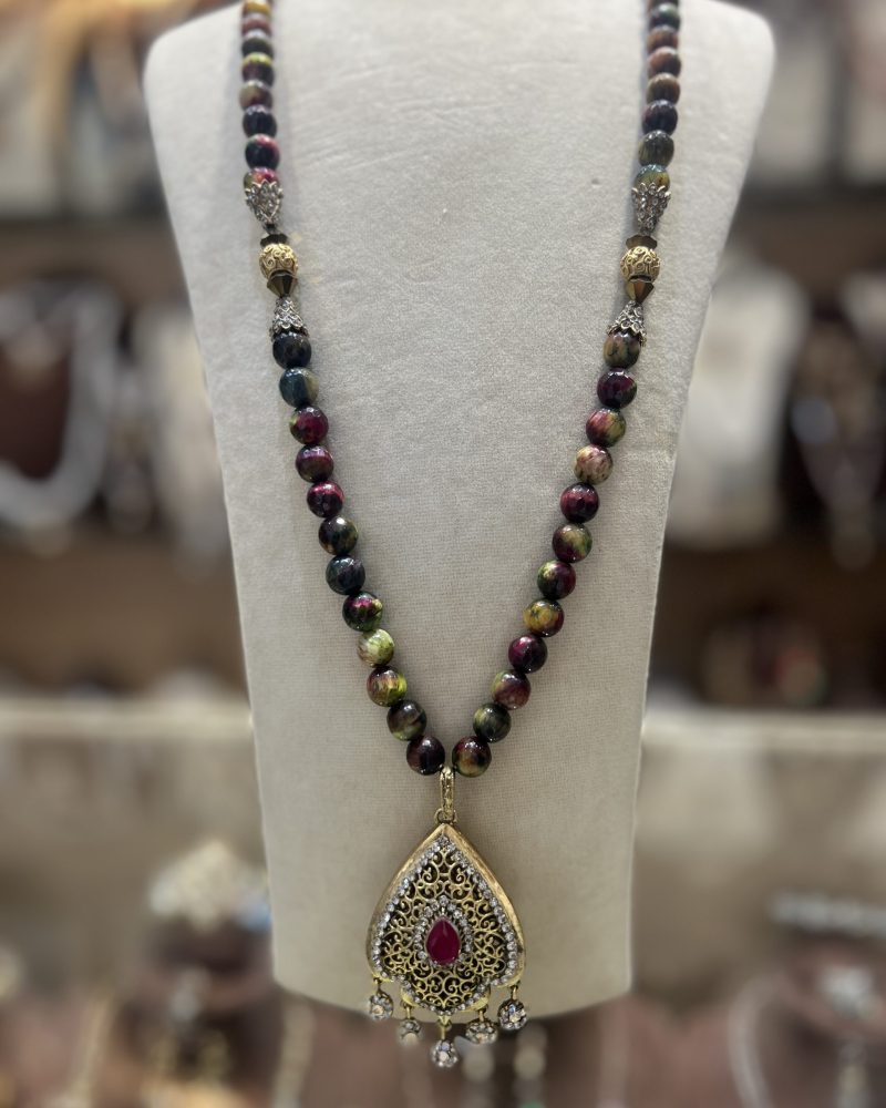 Sautoir Sultana en perles naturelles aux nuances bordeaux et vertes avec intermédiaires dorés ciselés et pendentif goutte à pierre centrale rouge,