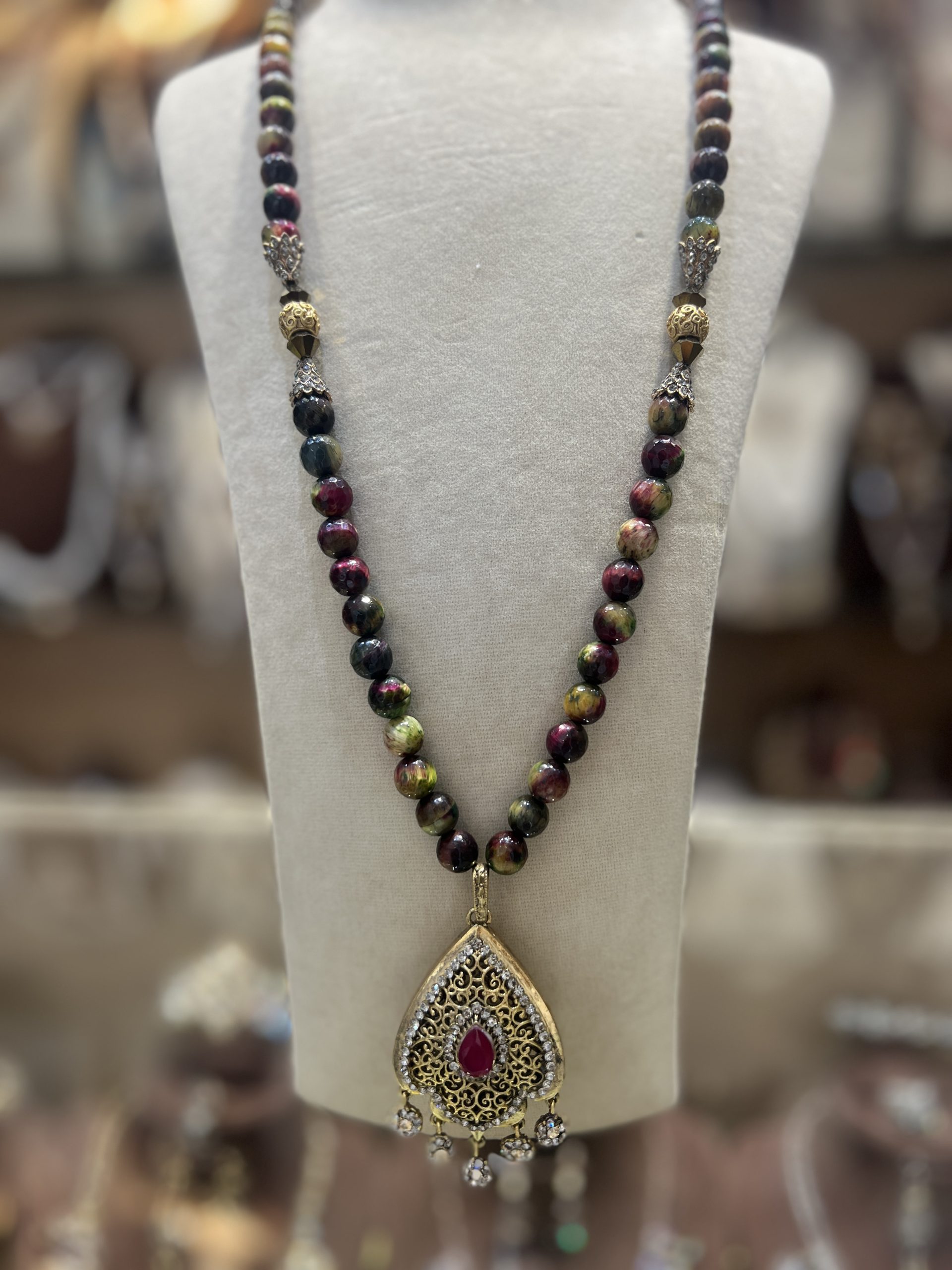 sautoir-sultana-perles-naturelles Sautoir Sultana en perles naturelles aux nuances bordeaux et vertes avec intermédiaires dorés ciselés et pendentif goutte à pierre centrale rouge,