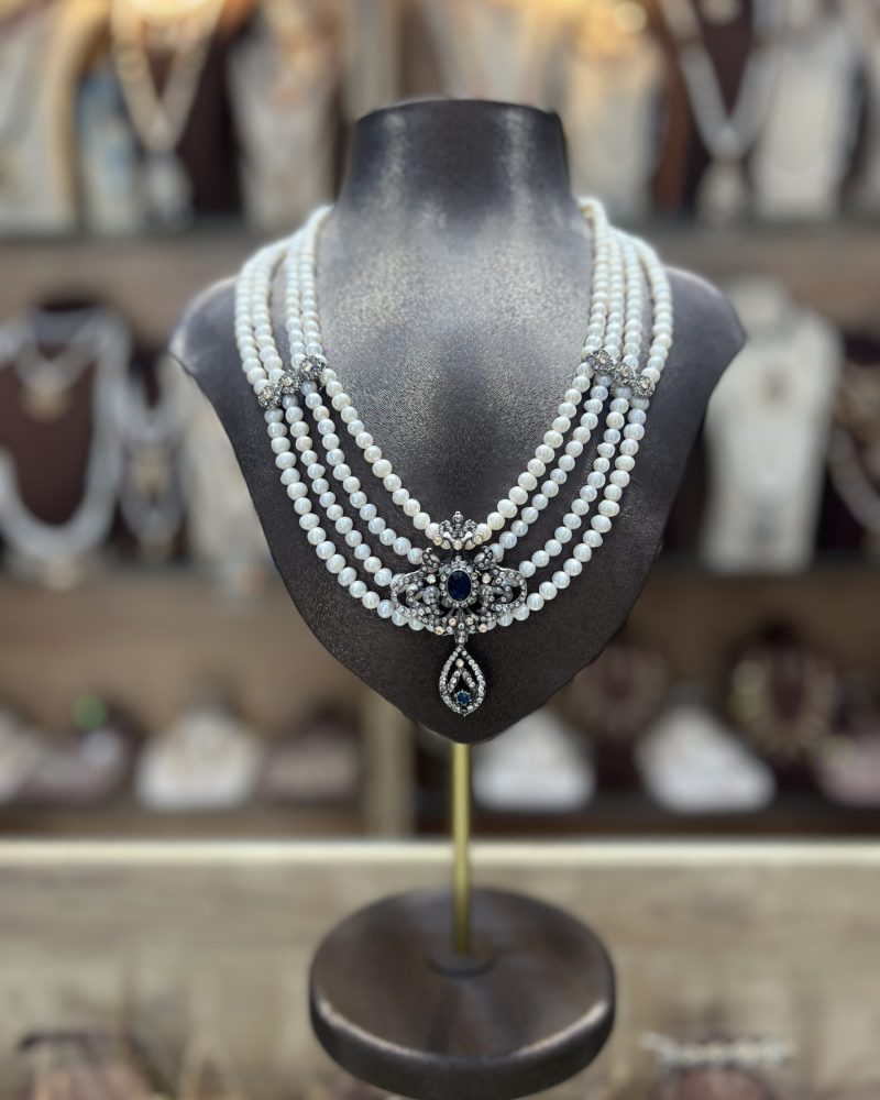 Collier Mkhebel Esmeralda Saphir à cinq rangs de perles de culture blanches avec intermédiaires ciselés et pendentif oriental serti d'une pierre bleue saphir, visible sur le fichier d'illustration.