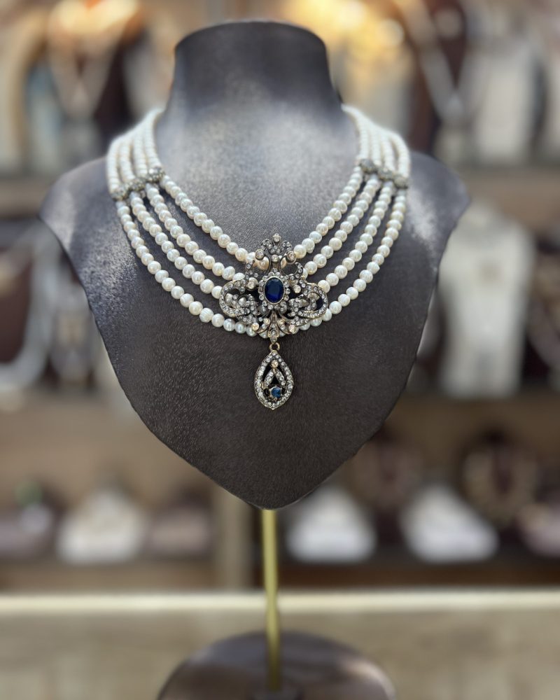 Collier Mkhebel Esmeralda Saphir Doré à cinq rangs de perles de culture blanches avec intermédiaires ciselés et pendentif oriental doré serti d'une pierre bleue saphir
