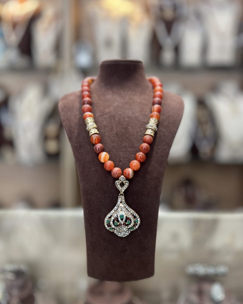 Sautoir en perles naturelles aux nuances ambrées et terracotta avec intermédiaires dorés ciselés et pendentif en forme de poire serti de zircons et pierres colorées