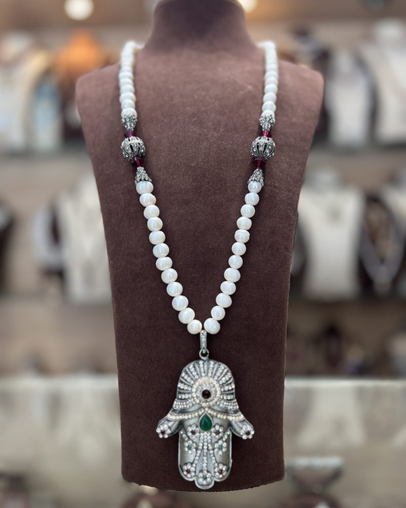 Sautoir Khamssa Royale en perles El Djohar nacrées blanches avec boules argentées ciselées, cristaux bordeaux et pendentif Main de Fatma serti de zircons, émeraude et rubis