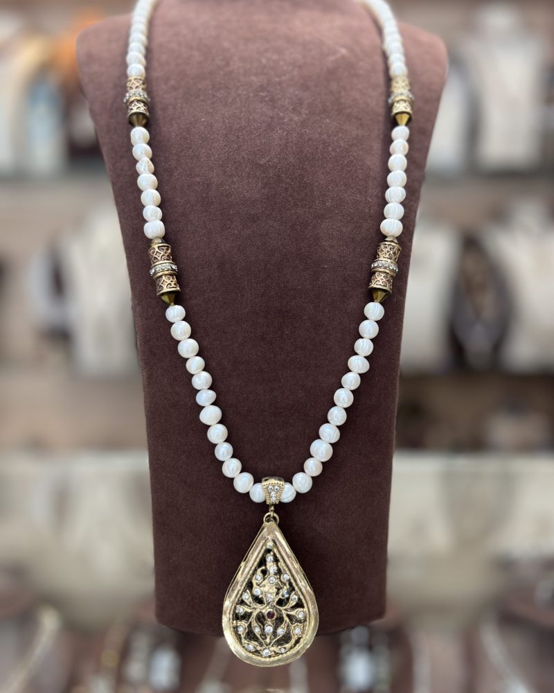 Sautoir La Meskia Classique Dorée en perles El Djohar nacrées blanches avec cylindres en bronze doré et pendentif poire ajouré serti de cristaux
